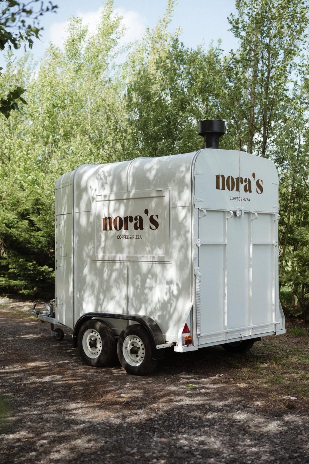 Nora’s white pizza trailer parked among the trees