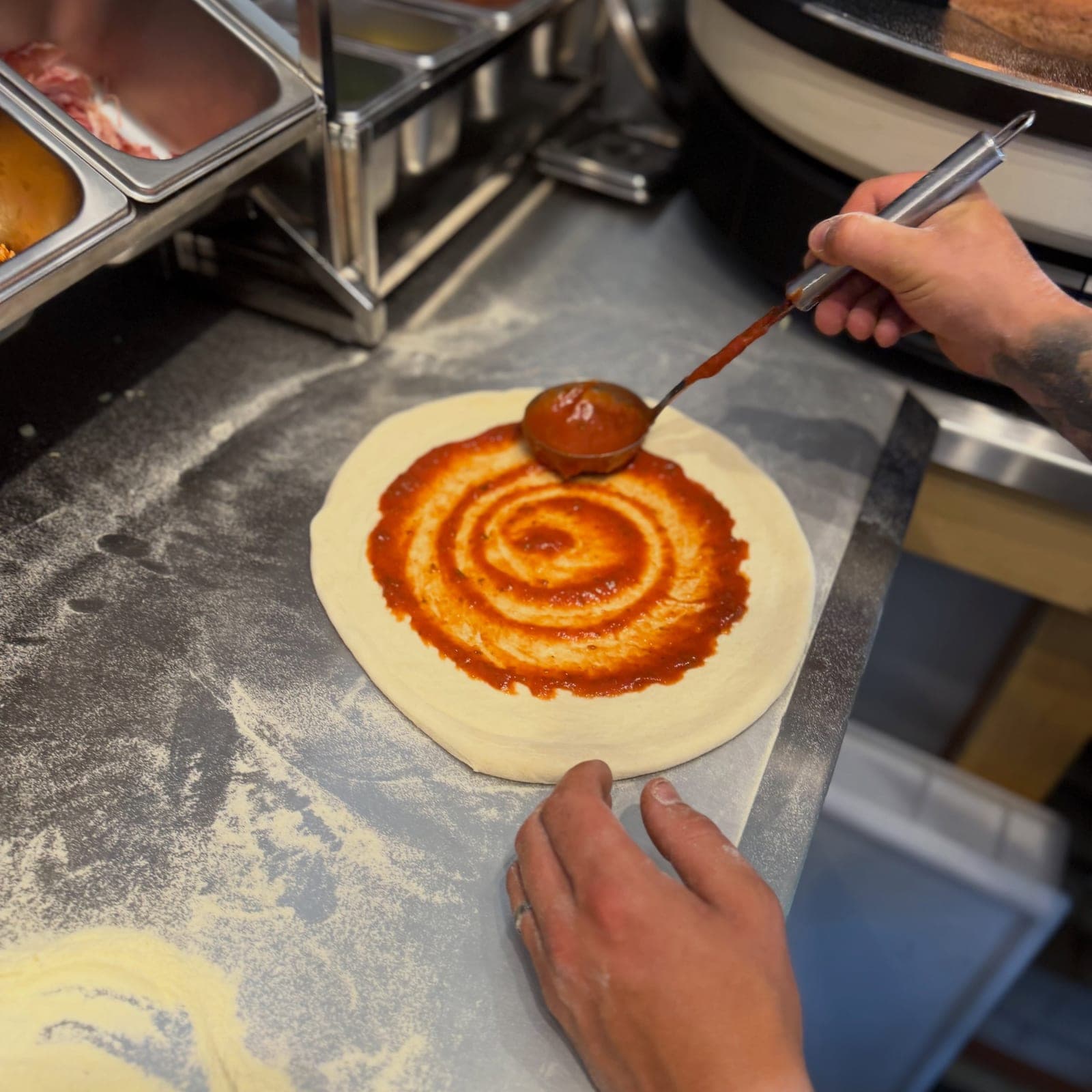 Spreading tomato sauce over a fresh sourdough pizza base
