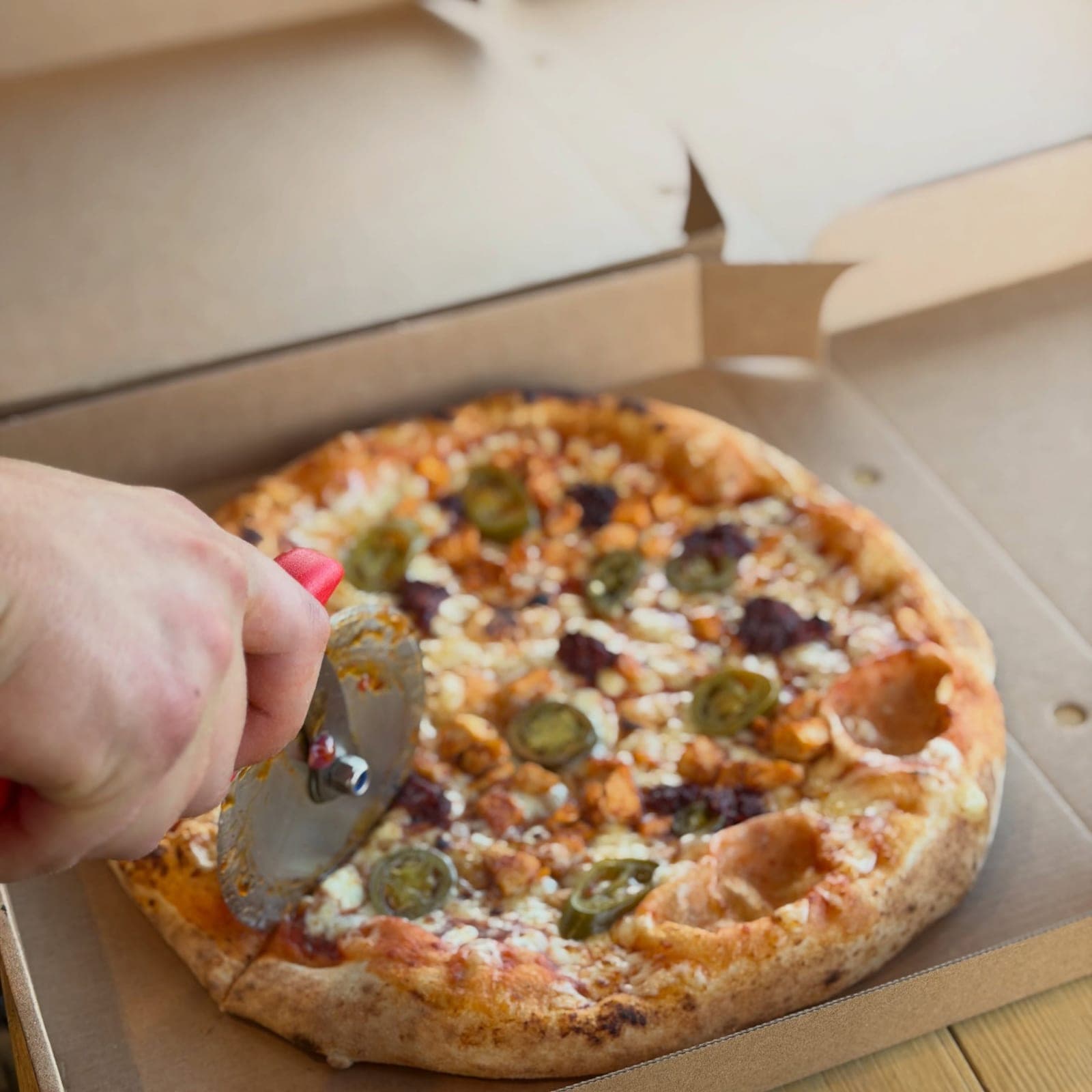 Slicing a spicy sourdough pizza topped with chicken and jalapeños